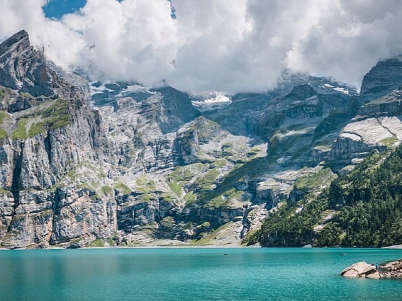 Turquoise alpine lake with forested slopes and a small lakeside town reflected in still water
