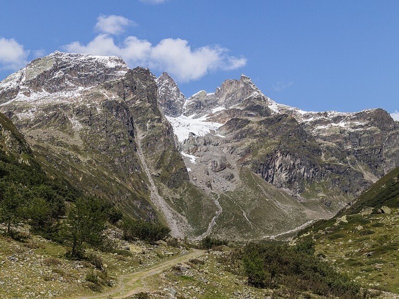 Forested alpine valley in winter with snow-covered peaks and ski runs above the treeline